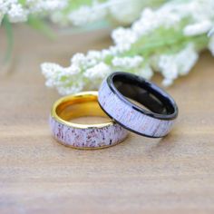 two wedding rings sitting next to each other on top of a wooden table with flowers in the background