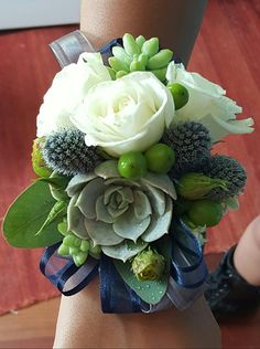 a woman's arm with a bouquet of flowers on top of it and green leaves around the wrist