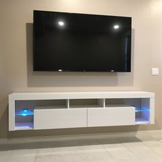 a large flat screen tv mounted to the wall above a white entertainment center with blue lights