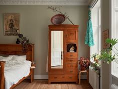 a bedroom with a bed, dresser and mirror in it's corner next to a window