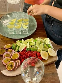 a wooden table topped with sliced fruit and veggies next to glasses filled with water