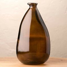 a brown glass vase sitting on top of a wooden table next to a white wall