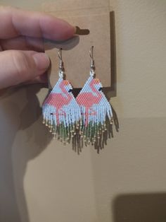 a pair of earrings with flamingos on them hanging from a hook in front of a wall