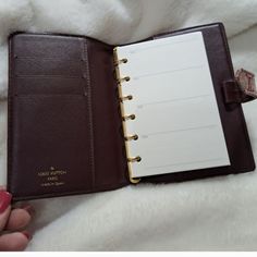 a woman's hand holding an open brown leather planner book on top of a white blanket