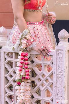 a woman in a pink and white lehenga standing on a fence with flowers