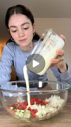 a woman pouring milk into a bowl filled with vegetables