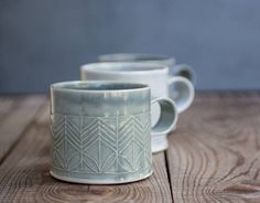 three white coffee mugs sitting on top of a wooden table next to each other