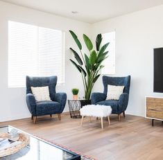 a living room with two blue chairs and a white ottoman in front of a flat screen tv