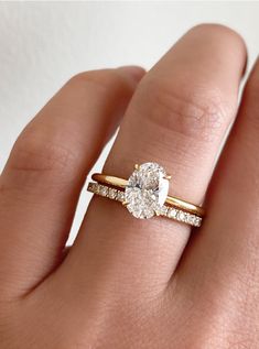 a woman's hand with two engagement rings on top of her finger and the ring has a pear shaped diamond in it