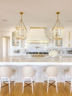 a large kitchen with white cabinets and gold accents on the hood over the stove is surrounded by three stools