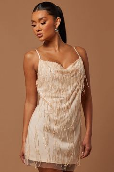 a woman wearing a dress with fringes on the bottom and one shoulder, standing in front of a brown background