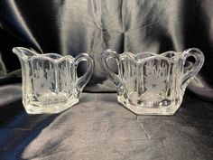 two clear glass pitchers sitting on top of a black cloth