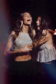 two young women laughing and dancing together at a party in the dark, with one holding her arm around the other's shoulder