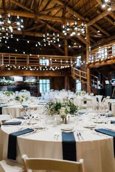 tables and chairs are set up for a wedding reception in a barn with lights strung from the ceiling