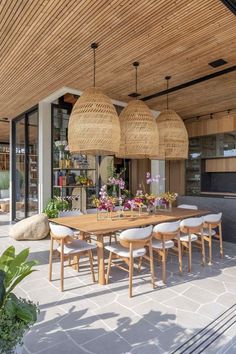 a wooden table surrounded by white chairs and wicker hanging from the ceiling above it