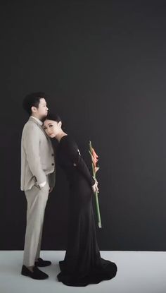 a man and woman standing next to each other in front of a black wall holding flowers