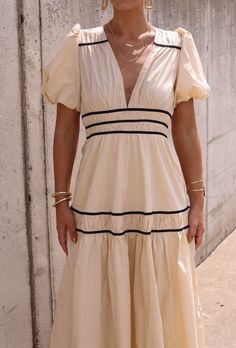 a woman in a white dress is standing by a wall with her hands on her hips