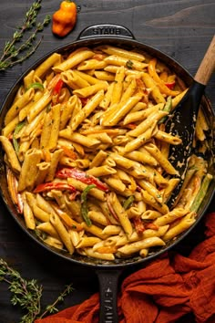 a pan filled with pasta and vegetables on top of a wooden table next to an orange towel