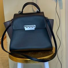 Brand New Zac Posen Tote Bag. 2 Toned - Black Base With Dark Taupe Sides. Side Flaps Can Be Tucked In Or “Winged Out” So It’s Like 2 Bags In One. Top Handle With Additional Removable Shoulder Strap. Metal Buckle Closure. Gun Metal Round “Feet” On The Bottom. Measures About 11inches High (14” To Top Of Handle). About 5.5 Inches Deep. Comes With Zac Posen Branded Dust Bag. Formal Gray Top Handle Bag, Formal Gray Bag With Silver-tone Hardware, Luxury Gray Evening Bag, Elegant Gray Crossbody Shoulder Bag, Gray Luxury Shoulder Bag For Evening, Formal Gray Bag With Detachable Strap, Gray Formal Satchel Bag, Modern Gray Formal Bag, Evening Top Handle Satchel With Gunmetal Hardware