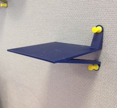 a blue shelf mounted to the side of a wall with two yellow pegs on it