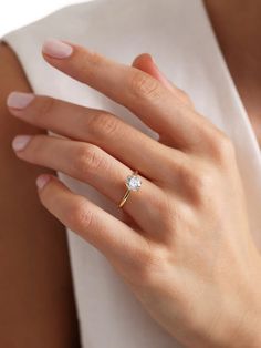 a woman's hand with a diamond ring on her left hand, wearing a white shirt