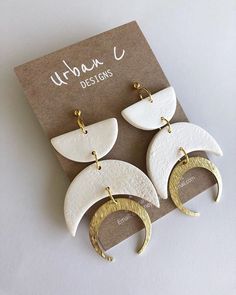 two white and gold moon shaped earrings on top of a brown card with the words urban designs written below it