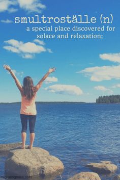 a woman standing on top of a rock next to the ocean with her arms outstretched