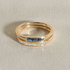 two gold wedding bands with blue and white stones on the sides, set against a beige background