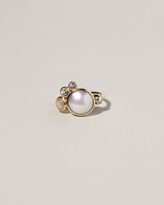 an image of a ring with pearls and stones on the front, sitting on a white surface