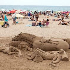 a horse sand sculpture sitting on top of a sandy beach next to the ocean and people