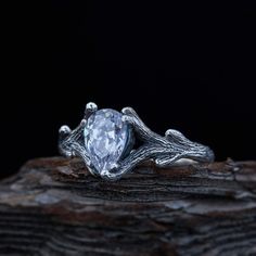 a white diamond ring sitting on top of a piece of driftwood with vines around it