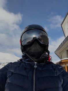 a person wearing a helmet and goggles standing in front of a snow covered building