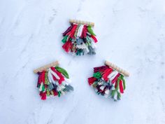 three small pieces of colorful fabric sitting on top of snow covered ground next to two wooden pegs