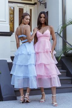 two beautiful women standing next to each other in front of a building wearing dresses with ruffles