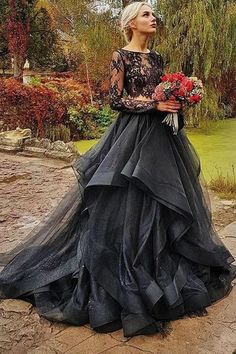 a woman in a long black dress standing on the ground with flowers and trees behind her