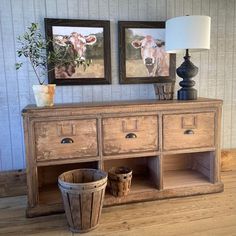 an old dresser with two pictures on the wall and a basket in front of it