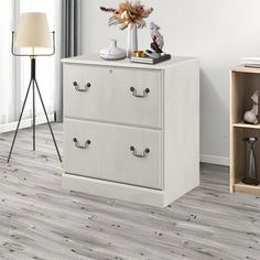 a white dresser with two drawers and a lamp next to it on top of a hard wood floor