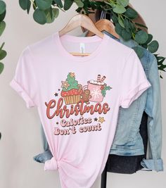 Funny Christmas graphic tee for women with the playful message 'christmas calories don't count'. Perfect for adding a touch of humor to the holiday season and a great conversation starter at festive gatherings. Ideal for women who enjoy celebrating Christmas with a bit of fun and lightheartedness. Product features - Side seams for structural support - Ribbed knit collar for elasticity - Shoulder tape for stability - Made with lightweight, breathable cotton - Ideal retail fit for casual and semi- Christmas Calories Don't Count, Food Shirt, Celebrating Christmas, Christmas Trends, Christmas Vibes, Retro Font, Women Humor, Tees For Women, Christmas Tees