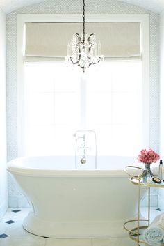 a white bath tub sitting next to a window with a chandelier hanging above it