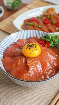 two bowls filled with fish and vegetables on top of a wooden table next to chopsticks