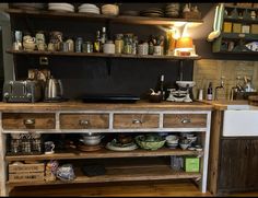 an old fashioned kitchen with lots of dishes on the counter and shelves in front of it