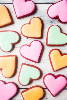 heart shaped cookies are arranged on a white wooden table with pink, yellow and green frosting