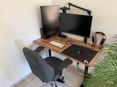 a computer desk with a monitor, keyboard and headphones on it next to a potted plant