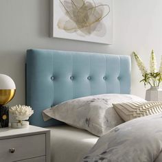 a blue headboard in a white bedroom with flowers on the nightstand and bed linens