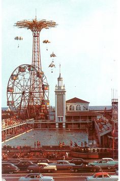 an amusement park with cars parked in front of it and people on the boardwalk below