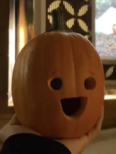 a person holding a carved pumpkin in front of a window with the face of a smiling pumpkin on it