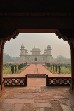 an archway leading to a large building in the middle of a field with trees and bushes