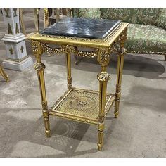 a table with a black marble top and gold trimmings on the legs, sitting in front of a couch