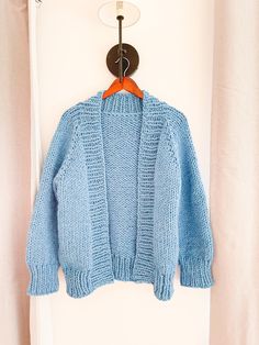 a blue knitted sweater hanging on a white wall next to a coat hanger