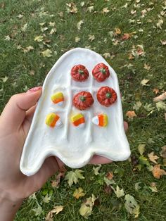 a hand holding a white plate with candy corn and candies on it in the shape of a ghost